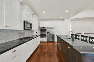 Kitchen with appliances with stainless steel finishes, a breakfast bar, white cabinetry, dark wood-type flooring, and recessed lighting