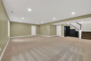 Basement unfurnished living room with light colored carpet, recessed lighting, and stairs