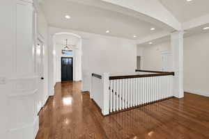 Corridor featuring dark wood finished floors, arched walkways, recessed lighting, and an upstairs landing