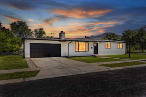 Ranch-style house featuring a garage, concrete driveway, a front lawn, and a chimney