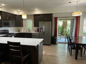 Kitchen with stainless steel appliances, light countertops, light wood-type flooring, hanging light fixtures, and a kitchen bar