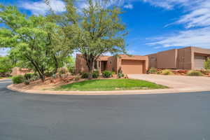 Adobe home featuring an attached garage, driveway, stucco siding, and a front lawn