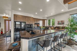 Kitchen featuring black appliances, recessed lighting, exhaust hood, a breakfast bar area, and plenty of natural light