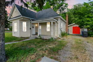 View of front of property with covered porch, a storage shed, roof with shingles, a chimney, and a yard