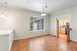 Unfurnished dining area with light wood-style flooring, a textured ceiling, and ornamental molding