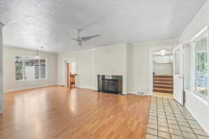 Unfurnished living room with light wood finished floors, ceiling fan, stairway, a fireplace with flush hearth, and crown molding