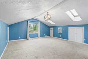Bonus room with a skylight, vaulted ceiling, a wall mounted air conditioner, a textured ceiling, and carpet floors
