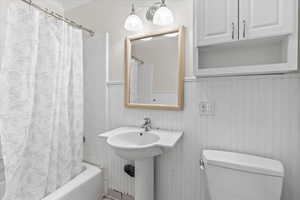 Full bathroom featuring a wainscoted wall and shower / bath combination with curtain