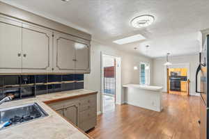 Kitchen featuring a skylight, appliances with stainless steel finishes, light countertops, light wood finished floors, and ornamental molding