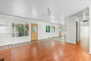 Unfurnished living room with wood finished floors, ceiling fan, plenty of natural light, crown molding, and a textured ceiling