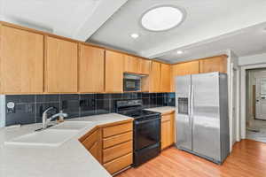 Kitchen with black appliances, light countertops, beamed ceiling, light wood-style floors, and decorative backsplash