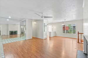 Unfurnished living room featuring a glass covered fireplace, wood finished floors, ceiling fan, and a textured ceiling