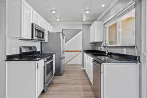 Kitchen featuring stainless steel appliances, dark stone countertops, light wood-style floors, white cabinetry, and crown molding