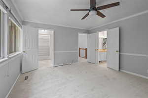 Unfurnished bedroom featuring a walk in closet, light carpet, ornamental molding, a ceiling fan, and ensuite bath