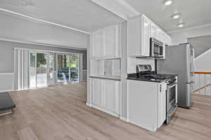 Kitchen with appliances with stainless steel finishes, crown molding, white cabinetry, light wood-style floors, and a textured ceiling
