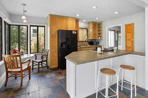 Kitchen featuring open shelves, a breakfast bar, black appliances, stone tile floors, and recessed lighting