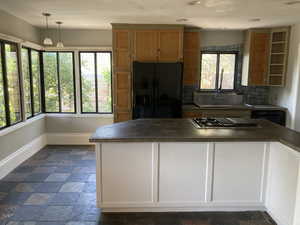 Kitchen with black refrigerator with ice dispenser, stovetop with downdraft, dark countertops, and healthy amount of natural light