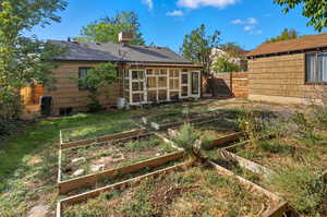 Rear view of house featuring a vegetable garden, a sunroom, and a shingled roof