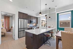 Kitchen featuring stainless steel appliances, dark brown cabinets, a breakfast bar area, light wood-type flooring, and a peninsula