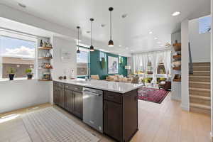 Kitchen featuring stainless steel dishwasher, a peninsula, dark brown cabinetry, light countertops, and open floor plan