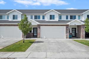 Townhome / multi-family property with board and batten siding, an attached garage, concrete driveway, and brick siding