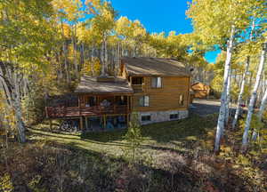 Back of house with a wooden deck, a yard, a view of trees, roof with shingles, and an outbuilding
