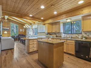 Kitchen with black dishwasher, log walls, light brown cabinets, a center island, and wood ceiling