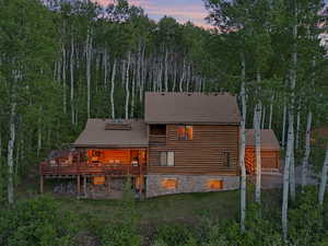 Back of property at dusk featuring roof with shingles, a wooden deck, log siding, and a lawn