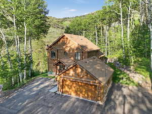 View of front of house with log siding, a view of trees, and driveway