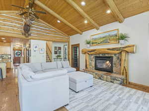 Living room with a wooden ceiling with exposed beams, light wood-type flooring, stairs, a fireplace, and ceiling fan