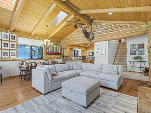Living area featuring a wood ceiling with exposed beams, a chandelier, wood finished floors, stairway, and a skylight