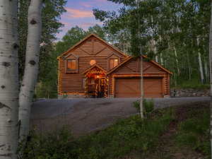 Log cabin featuring driveway, an attached garage, and log exterior