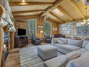 Living area featuring wooden ceiling, rustic walls, a skylight, a chandelier, and a stone fireplace