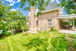 Back of property featuring a balcony, a patio, brick siding, a chimney, and a shingled roof