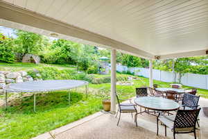 Fenced backyard featuring a trampoline, outdoor dining space, and a patio