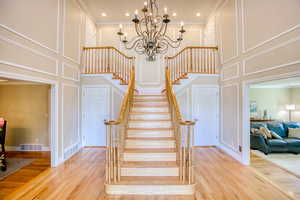 Stairway featuring a decorative wall, a towering ceiling, a chandelier, ornamental molding, and wood finished floors
