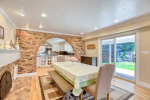 Dining area with plenty of natural light, arched walkways, light wood finished floors, brick wall, and crown molding