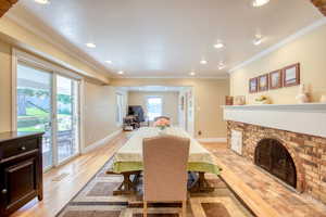 Dining area with light wood finished floors, crown molding, a fireplace, and recessed lighting