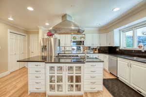 Kitchen featuring appliances with stainless steel finishes, island range hood, dark countertops, crown molding, and white cabinets