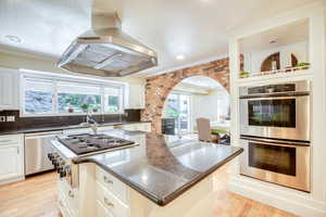 Kitchen featuring island exhaust hood, stainless steel appliances, arched walkways, crown molding, and healthy amount of natural light