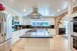 Kitchen featuring stainless steel appliances, island range hood, a center island, white cabinets, and crown molding