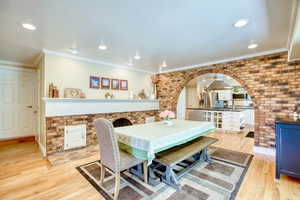 Dining space with arched walkways, light wood finished floors, recessed lighting, ornamental molding, and brick wall
