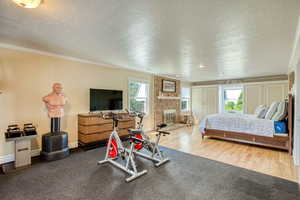 Primary bedroom featuring a textured ceiling, ornamental molding, wood finished floors, and a brick fireplace