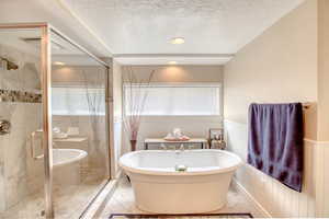 Bathroom featuring a freestanding bath, wainscoting, a textured ceiling, a stall shower, and marble finish flooring