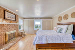 Primary bedroom featuring multiple windows, light wood-style floors, ornamental molding, a brick fireplace, and a textured ceiling