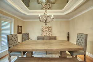 Dining area with a chandelier, a tray ceiling, wood finished floors, and crown molding