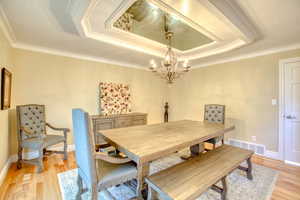Dining room with a raised ceiling, a chandelier, light wood-style flooring, and crown molding