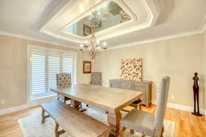 Dining area featuring a raised ceiling, a chandelier, ornamental molding, and light wood-style flooring