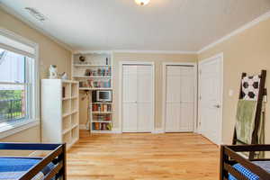 3rd Bedroom with two closets, a textured ceiling, light wood-style flooring, and ornamental molding