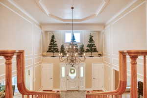 Foyer with a chandelier, a decorative wall, ornamental molding, and a raised ceiling